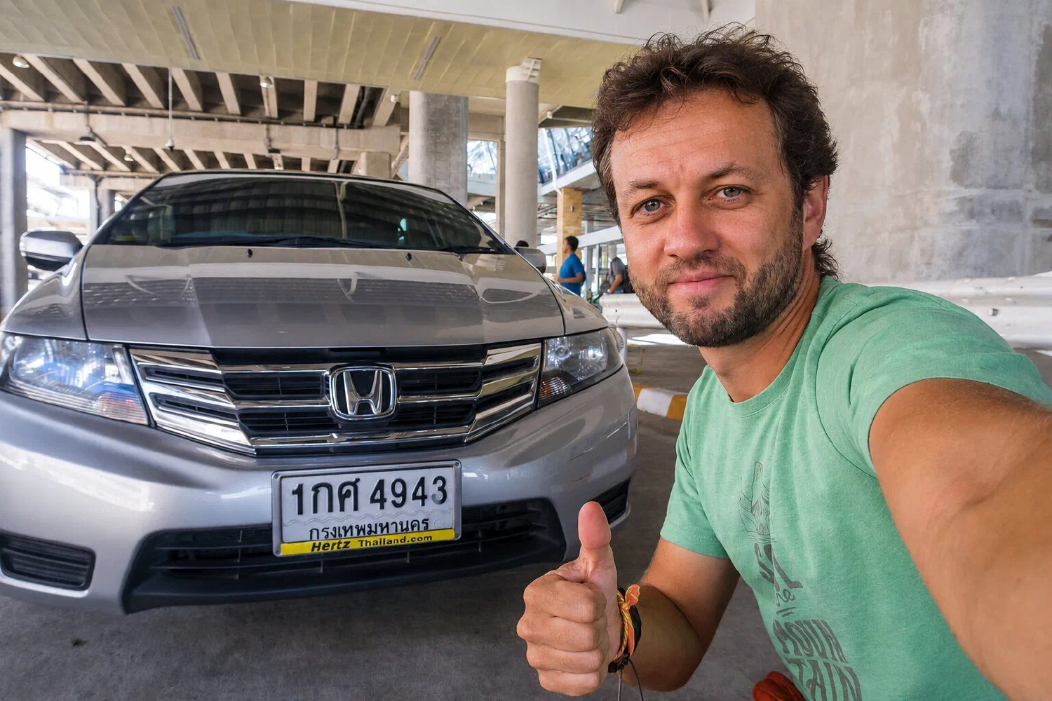 Мужчина рядом с арендованной Honda у стойки Hertz в Таиланде